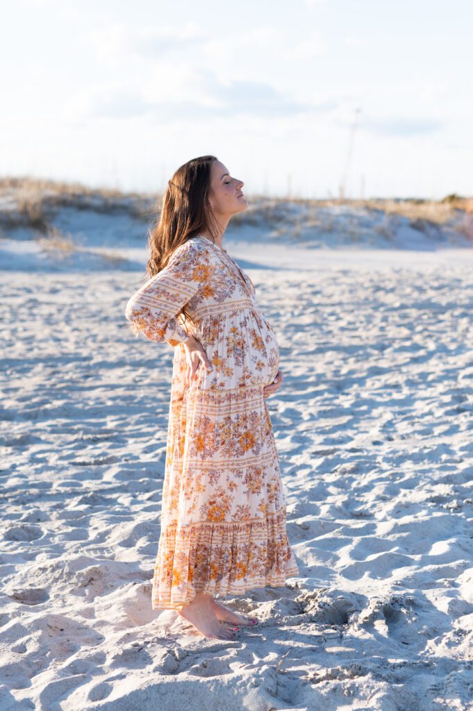 pregnant woman smiling towards the sun with eyes closed at the beach