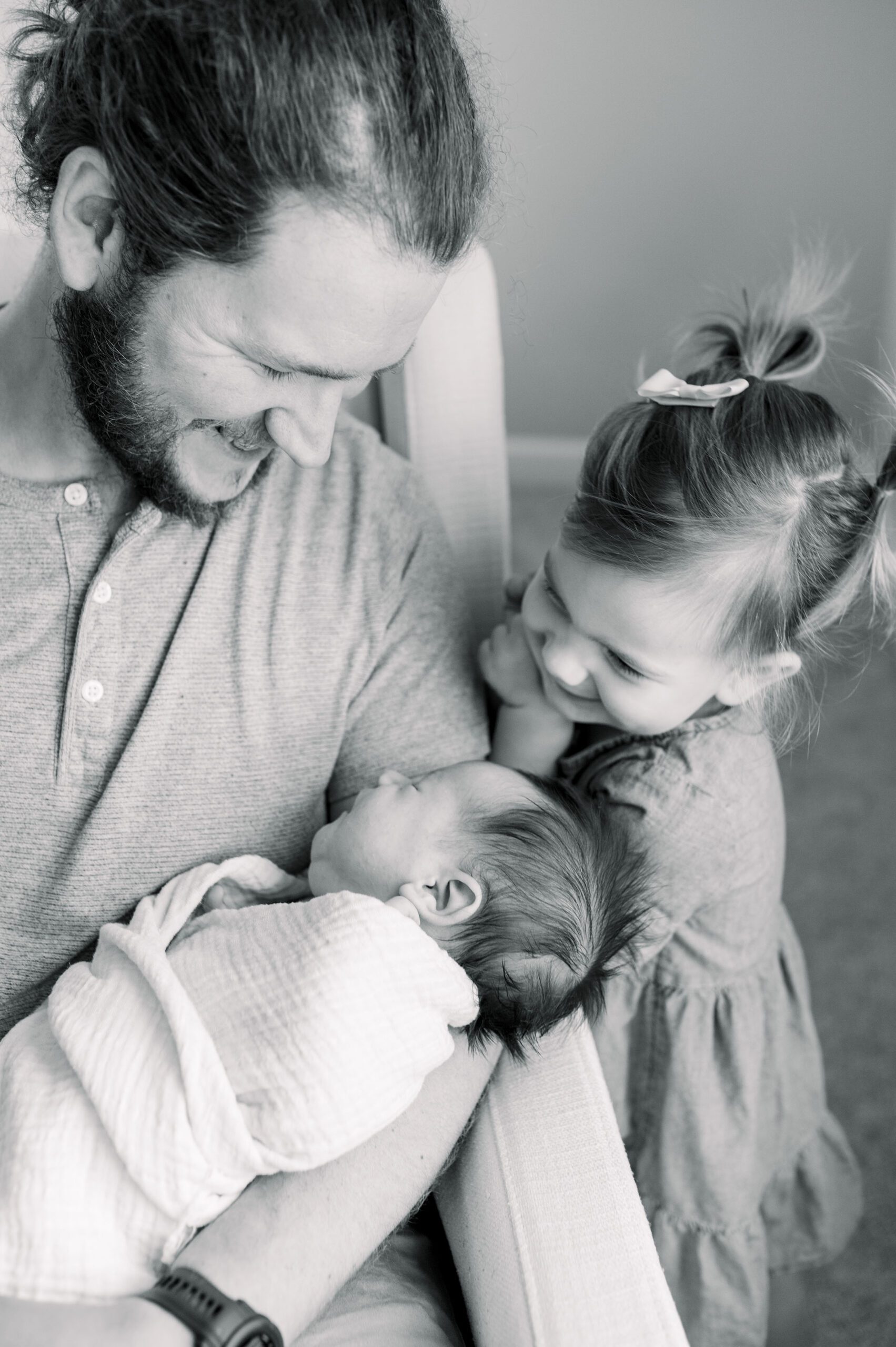 father and toddler smiling at swaddled baby